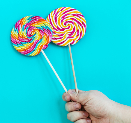 striped spiral multicolor Lollipop closeup in hand on blue backgroundの写真素材