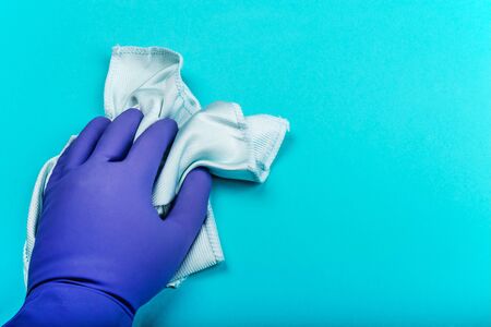 hand in a rubber glove holding a rag and wipes on a blue background. the concept of cleaning an apartment or homeの写真素材