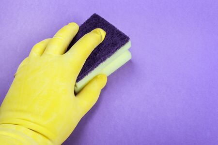 rubber-gloved hand holds a sponge and wipes the purple background. the concept of cleaning an apartment or houseの写真素材
