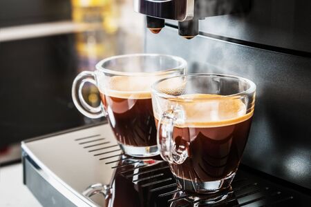 freshly brewed coffee is poured from the coffee machine into glass cupsの写真素材