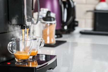 freshly brewed coffee is poured from the coffee machine into glass cupsの写真素材