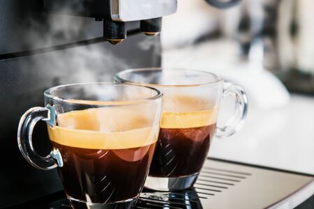 freshly brewed coffee is poured from the coffee machine into glass cups in the kitchen at homeの写真素材