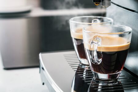 freshly brewed coffee is poured from the coffee machine into glass cups in the kitchen at homeの写真素材
