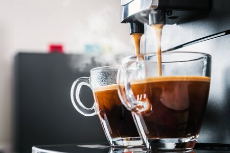 freshly brewed coffee is poured from the coffee machine into glass cups in the kitchen at homeの写真素材