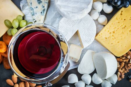 assorted cheeses, soft, hard, rennet and brine, and a glass of red wine. Focus on the glassの写真素材