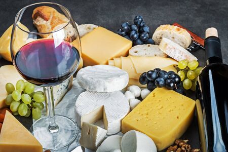 assorted cheeses, soft, hard, rennet and brine, and a glass of red wine. Focus on the glassの写真素材