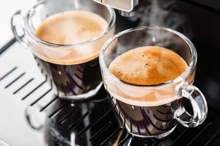 two cups of freshly brewed coffee in the coffee machineの写真素材
