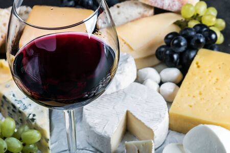 glass of red wine on the background of assorted cheeses, soft, hard, rennet and brine with fruits, nutsの写真素材