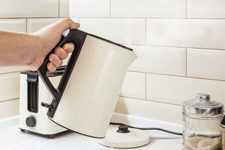 boiling teapot in hand on the background of kitchen utensils. Breakfastの写真素材