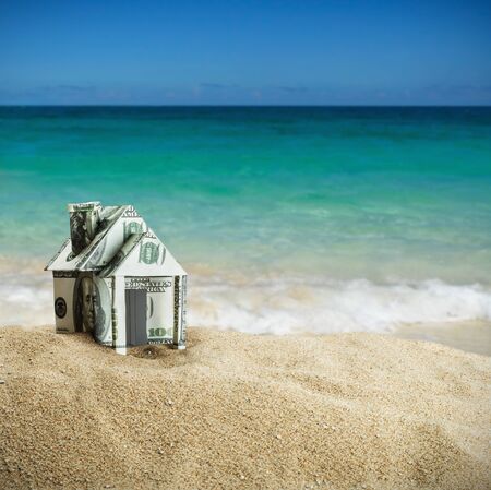 house cut out of dollar bills on the sand. Concept on the topic of selling or buying a home.の写真素材