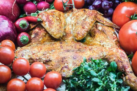 chicken tobacco cooked on the table with fresh vegetables and herbsの写真素材