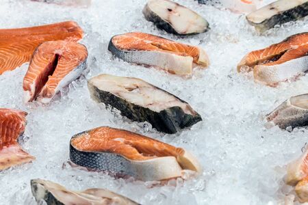 fillets and steaks of fish salmon and cod lie on the ice of a store counter or fish marketの写真素材