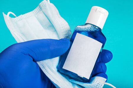 hand in rubber gloves holds personal protective equipment against covid-19 coronavirus. Antiseptic hand liquid, face mask and rubber glovesの写真素材