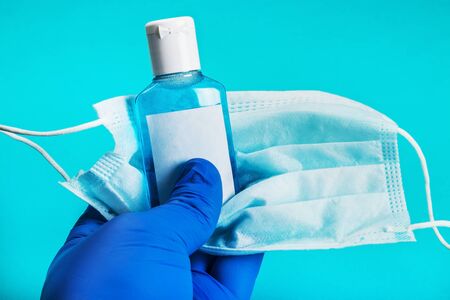 hand in rubber gloves holds personal protective equipment against covid-19 coronavirus. Antiseptic hand liquid, face mask and rubber glovesの写真素材