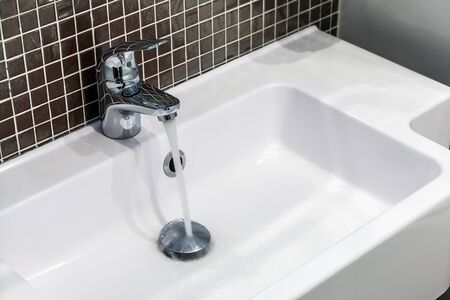 chrome faucet with running water in the toilet or bathroomの写真素材