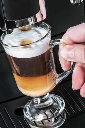 hot cappuccino from the coffee machine is poured into a glass Cupの写真素材
