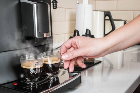 woman's hand takes a glass Cup of hot coffee from the coffee machineの写真素材