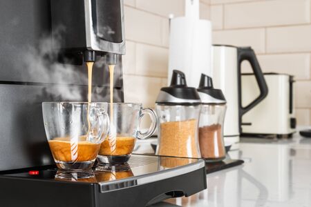 hot coffee from the coffee machine is poured into glass cupsの写真素材