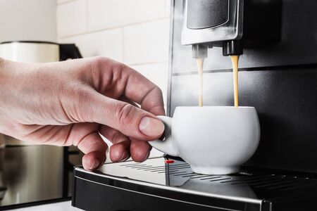 woman's hand picks up a white porcelain Cup of hot coffee from the coffee machineの写真素材
