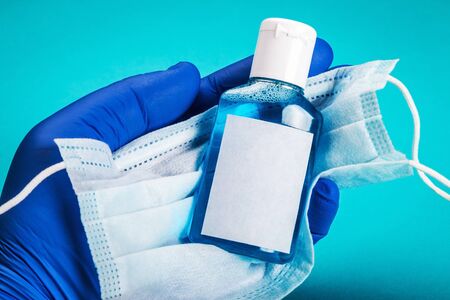hand in rubber gloves holds personal protective equipment against covid-19 coronavirus. Antiseptic hand liquid, face mask and rubber glovesの写真素材