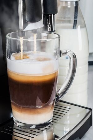 hot cappuccino from the coffee machine is poured into a glass Cupの写真素材