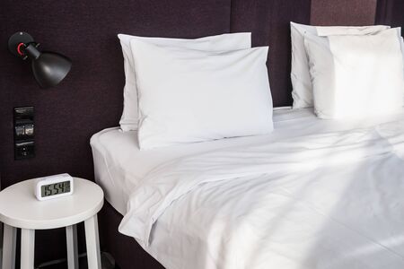 bed and bedside table with alarm clock in the hotel roomの写真素材