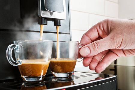 womans hand takes a glass Cup of coffee. Prepared coffee on the coffee machine is poured into glass cupsの写真素材