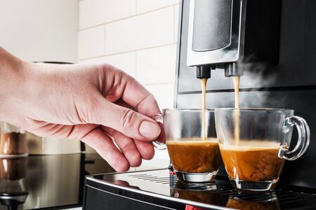 womans hand takes a glass Cup of coffee Prepared on the coffee machineの写真素材