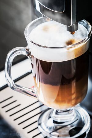 glass cup with hot cappuccino with foam prepared in the coffee machineの写真素材