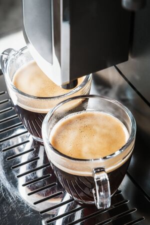 glass cups with hot coffee poured from the coffee machineの写真素材