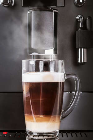 glass cup with hot cappuccino prepared in the coffee machineの写真素材