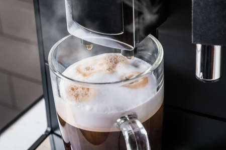 glass cup with hot cappuccino prepared in the coffee machineの写真素材