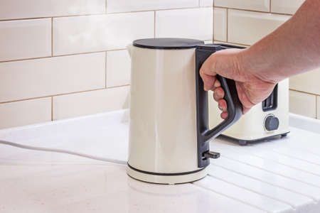 boiling electric kettle in hand in the kitchenの写真素材