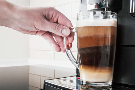hand picks up a glass of hot cappuccino with foam made in the coffee machineの写真素材