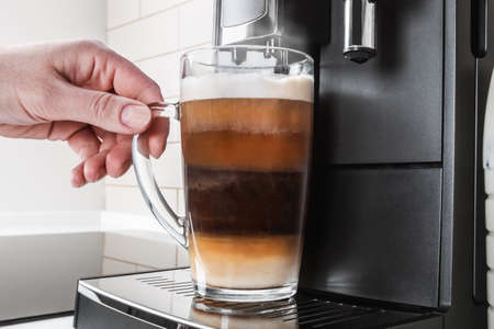 hand picks up a glass of cappuccino made in the coffee machine at homeの写真素材