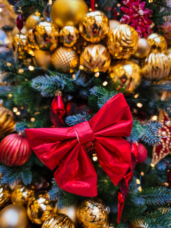 Beautifully decorated Christmas tree adorned with gold ornaments and a large red bow in a festive setting during holiday seasonの写真素材