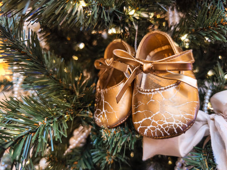 Elegant golden baby shoes hanging on a Christmas tree adorned with lights and decorationsの写真素材