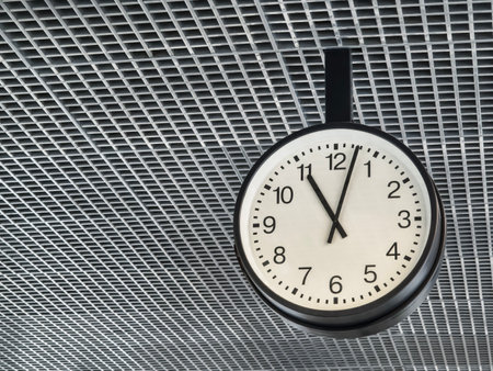 Wall clock displaying 12 oclock in a modern indoor space with a grid ceiling