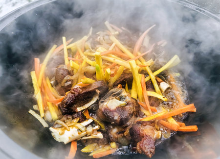 Cooking vegetables and meat in a pot over high heat in an outdoor setting with steam risingの写真素材