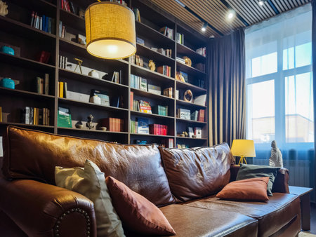 Cozy reading nook featuring a leather sofa and well-stocked bookshelf in a sunlit roomの写真素材