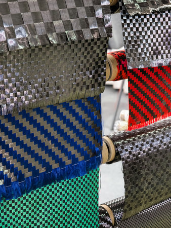 Various carbon fiber fabric samples displayed on rolls for material testing and selection in a manufacturing facilityの写真素材