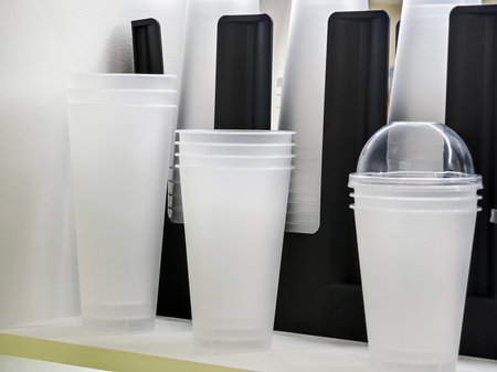 Various clear and opaque disposable cups displayed on a shelf in a cafe during daytime hoursの写真素材