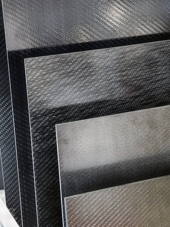 Variety of sleek carbon fiber sheets arranged in a stack showcasing different textures and colors in...