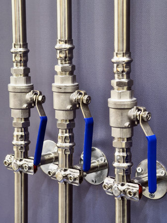 Detailed close-up of industrial piping system with blue handles showcasing valve mechanisms and stainless steel fittingsの写真素材