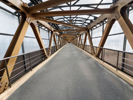 Modern pedestrian bridge spans over urban landscape in the heart of the city during a cloudy dayの写真素材