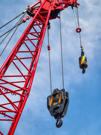 Heavy crane with pulleys lifting materials against a blue sky at a construction siteの写真素材