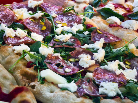 Fresh pizza topped with salami, cheese, and greens served on a wooden table in a busy restaurantの写真素材