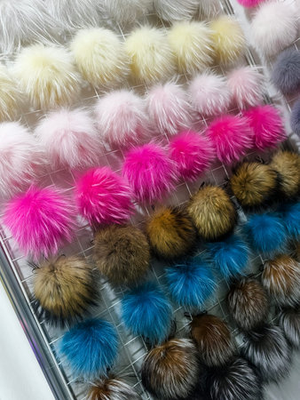 Display of colorful fur pom poms in a craft store showing various colors and sizes hanging in rows...