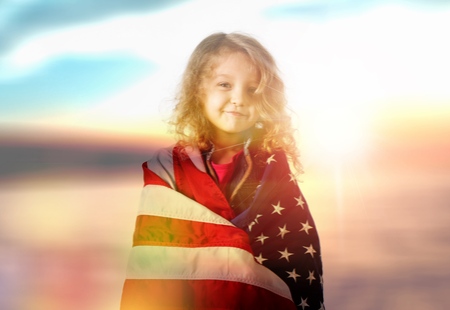 Patriotic holiday. Happy kid, cute little child girl with American flag. USA celebrate 4th of July.の写真素材