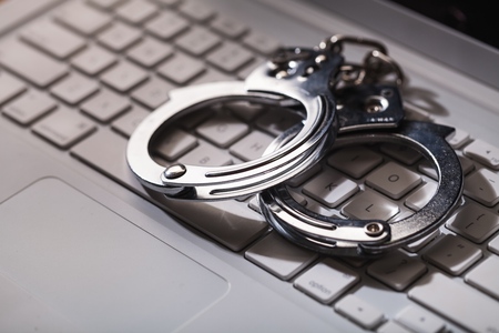 Selective focus on handcuffs on a keyboard cyber crime, hacking, bullying Against law concept in dark low key toneの写真素材